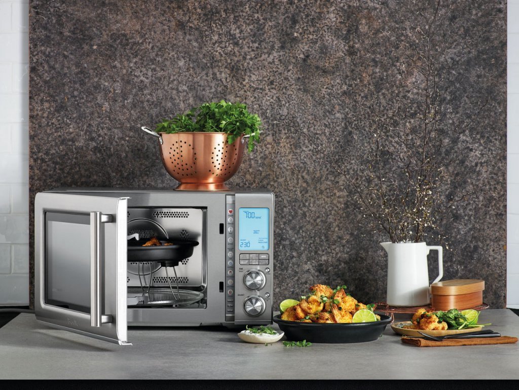 A person placing a covered ceramic dish into a modern microwave for heating.