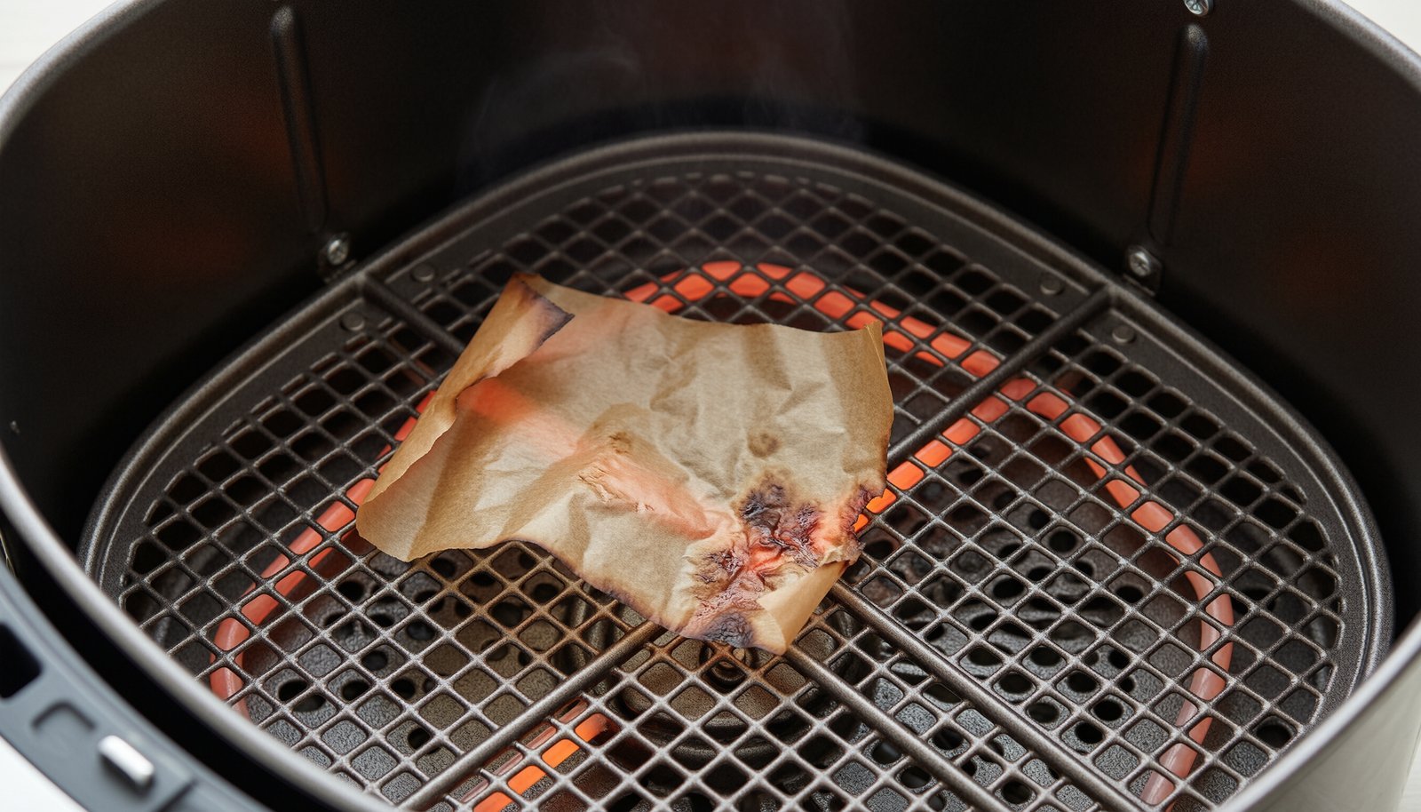 A piece of parchment paper caught in an empty air fryer heating element.