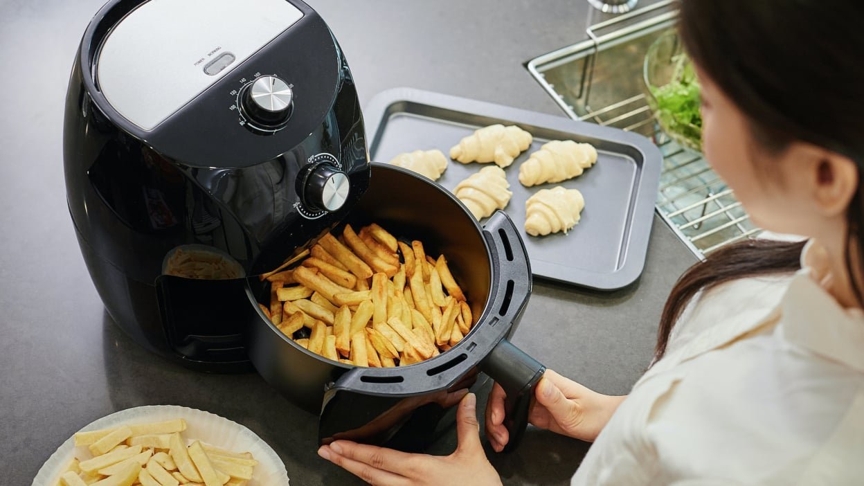 Close up of hands adjusting the digital settings on an air fryer control panel.