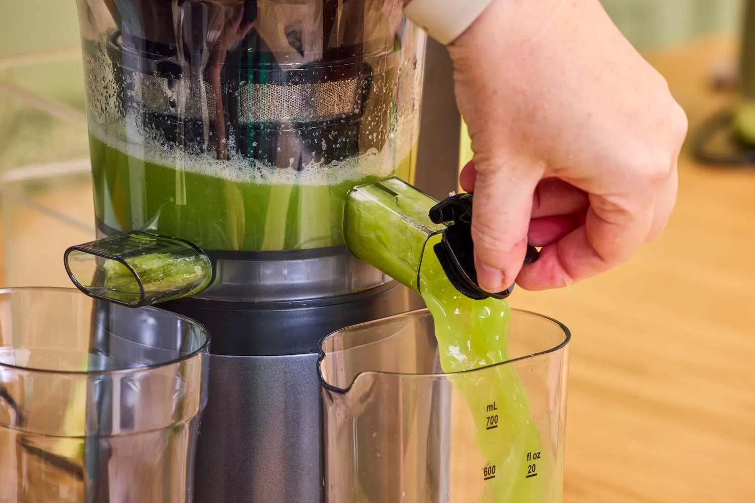 Fresh kale leaves being processed inside a slow masticating juicer in a bright kitchen.
