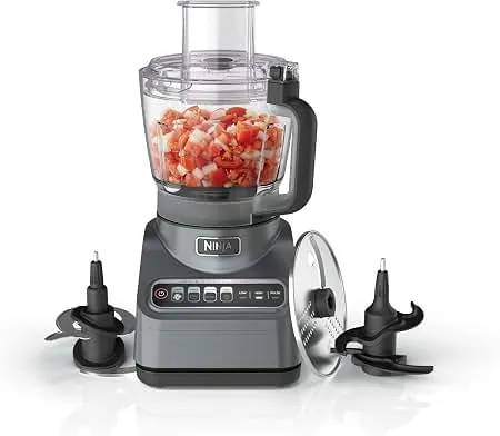 Hands rinsing a food processor bowl under a kitchen faucet before cleaning.
