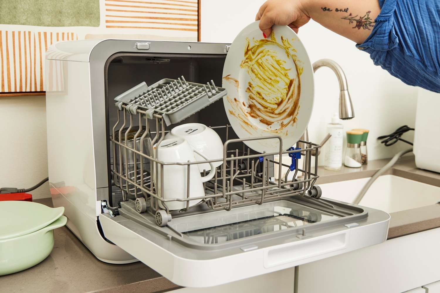 A modern portable dishwasher sits on a clean kitchen counter in a bright home.