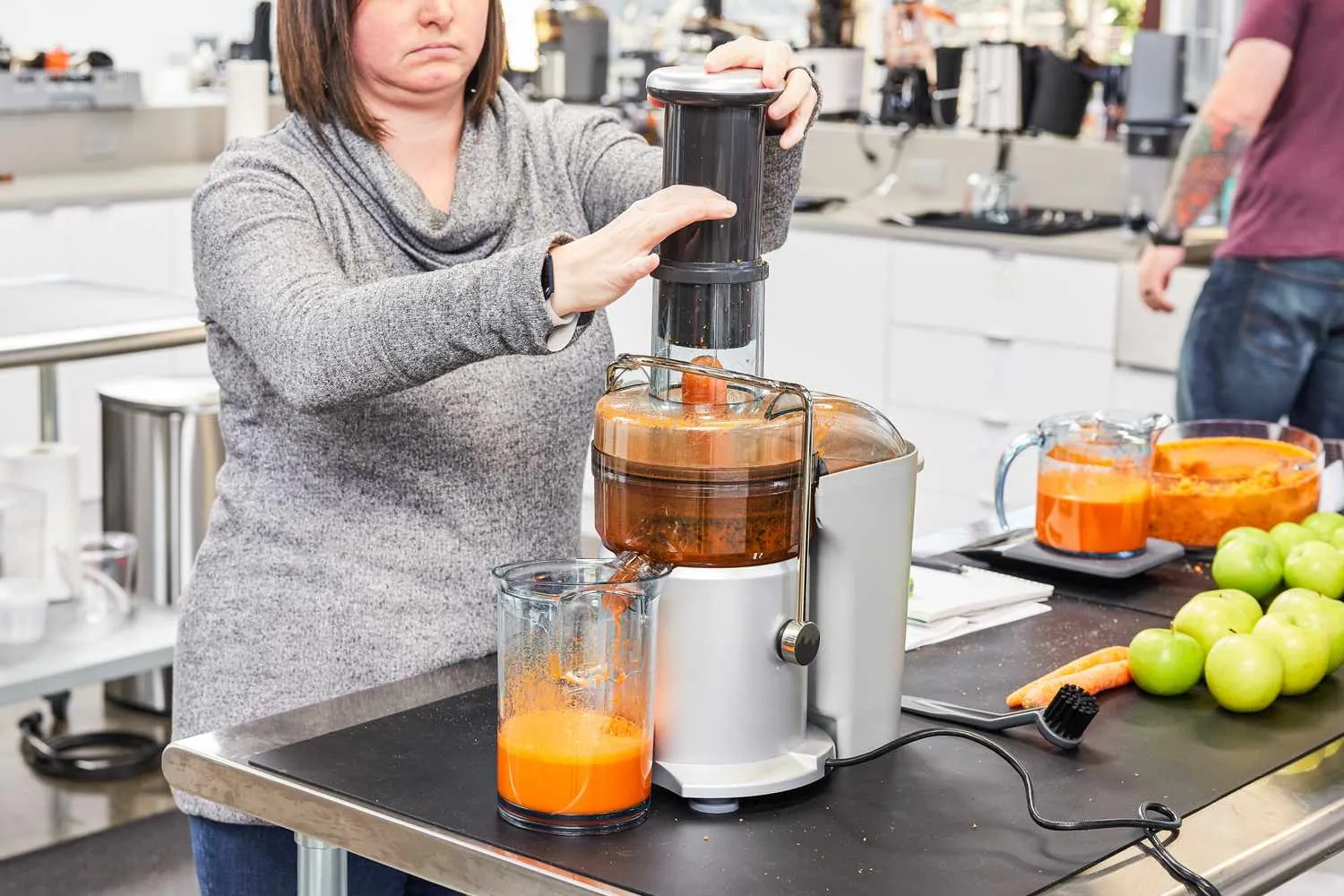 A person feeding sliced apples into a masticating juicer using a plastic pusher.